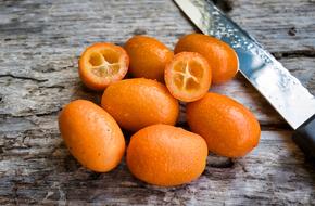 Beautiful, ripe, orange kumquats, near the shiny knife with liquid drops, on the wooden surface