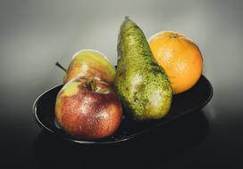 Beautiful still life with colorful apples, green pear and orange on the black plate