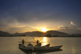 Fishermen on the boats on the beautiful waterscape at colorful and beautiful sunset, behind the mountains, in the province in Vietnam