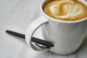 White cup of coffee with beautiful drawing, and with the black pen in the handle