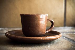 Beautiful, shiny, brown pottery cup, on the brown saucer, near the wall