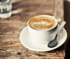 White cup of coffee with the beautiful drawing, with the spoon, on the saucer