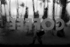 Black and white photo of the reversed "COFFEE" sign on the glass in rain drops