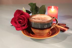 a cup of coffee, a rose and a burning candle