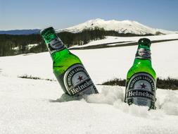 Green Heineken bottles, in the snow, on the beautiful mountains landscape