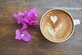 Beautiful, purple flowers and white cup of coffee with heart drawing