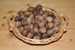 Beautiful, brown walnuts of different shades, in the beautiful wicker basket, on the wooden surface