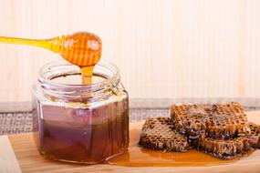 Beautiful honey in the glass jar, near the honeycombs, on the wooden board