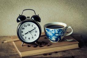 Beautiful and colorful still life with the blue and white cup of coffee, clock, pen and beans, on the book