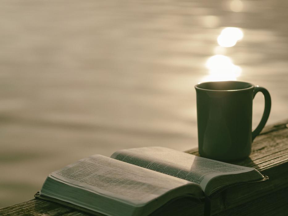 open book and mug near water on blurred background