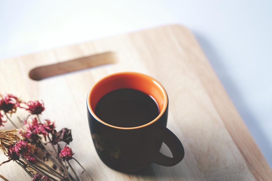 Coffee in dark cup and dry flowers on wooden board