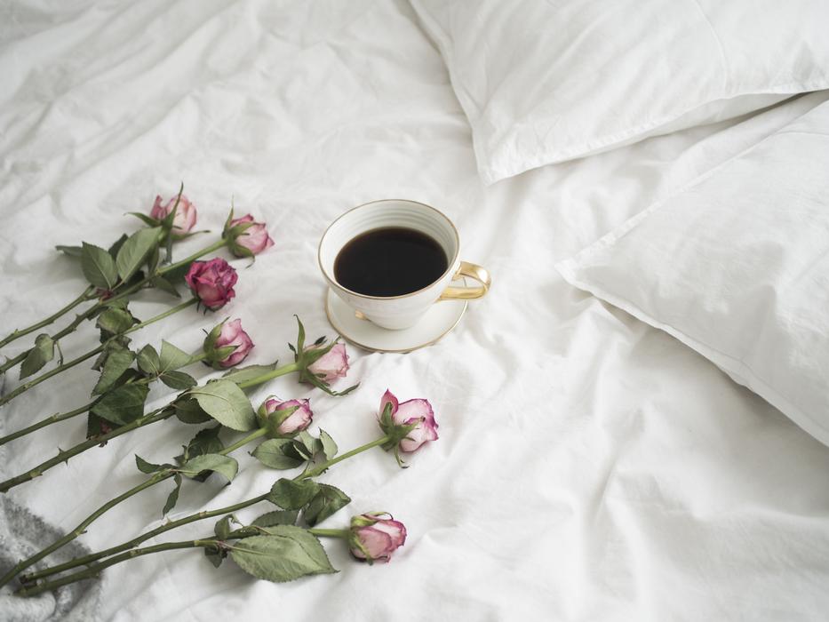 roses and a cup of coffee on a white bed
