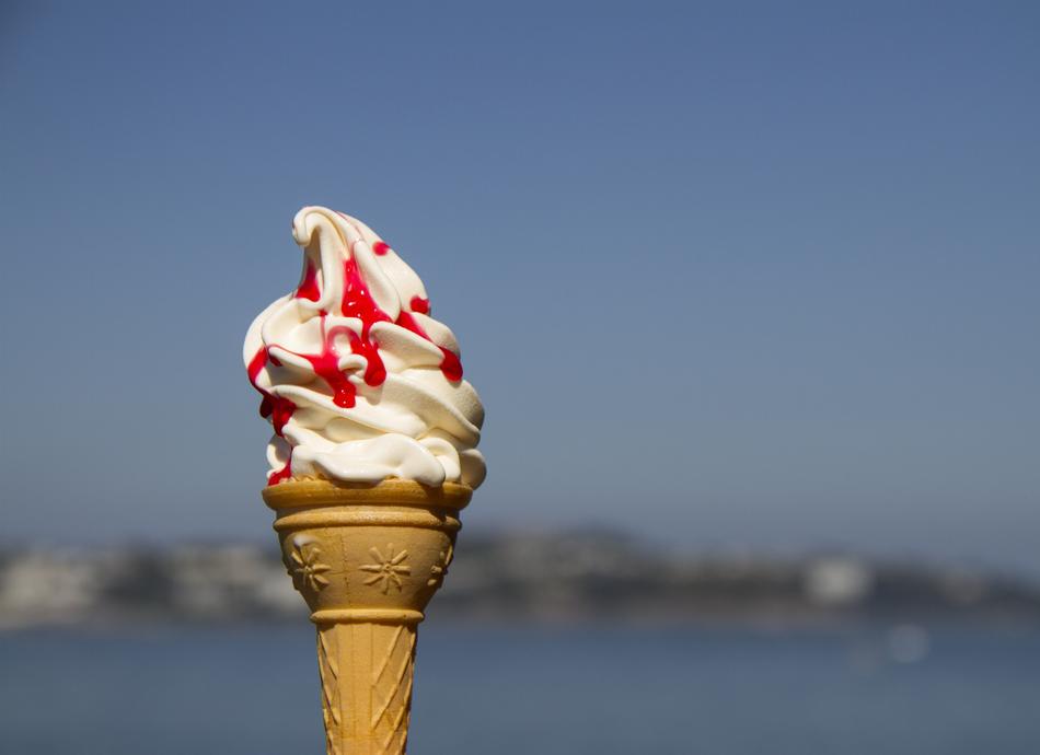 Close-up of the beautiful white ice cream in the cone, with the red topping, at background with the city on the shore