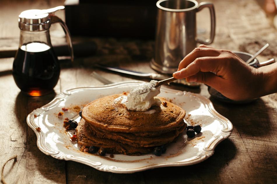 Person, spreading cream on the beautiful pancakes, near the drink