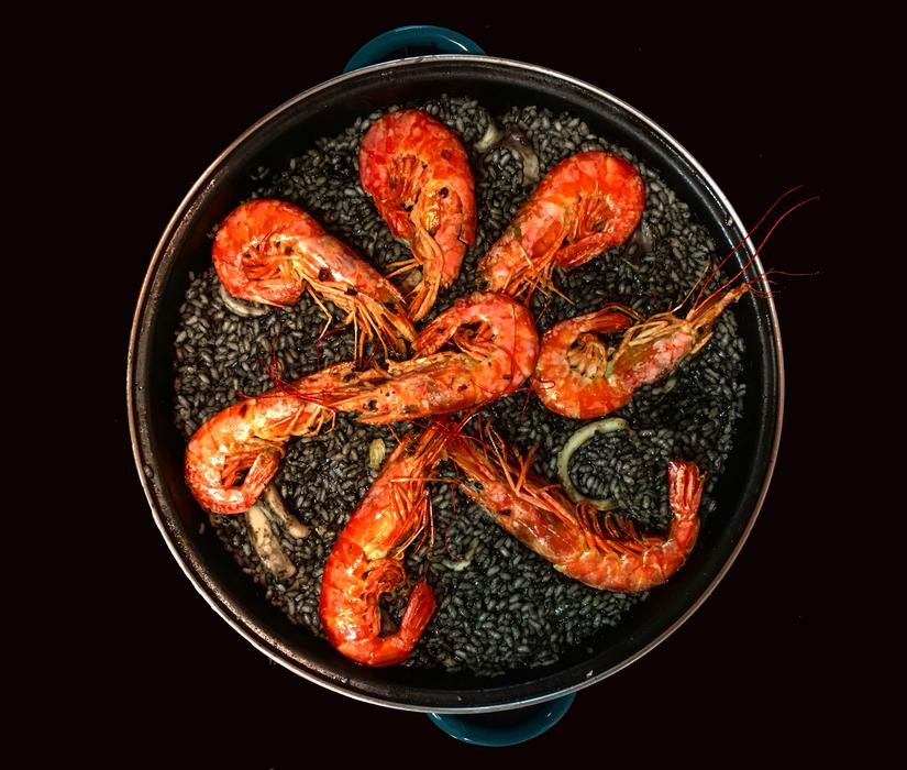Beautiful and colorful paella with the black rice and shrimps, on the black surface