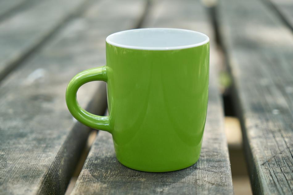 green cup on the garden table close-up on blurred background