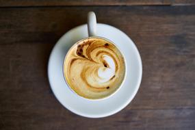 Top view of the cup of the beautiful coffee, with the beautiful drawing, on the saucer, on the wooden table