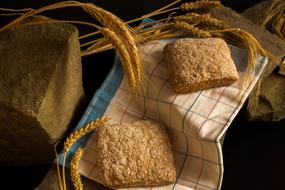 Beautiful bread on the colorful cloth, near the wheat and rock, in light