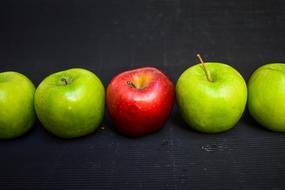 Beautiful red and green apples in row, on the black surface