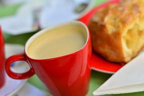 Beautiful, red cup of coffee, near the dessert on the red plate