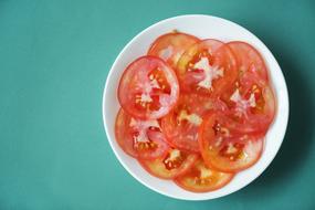 Beautiful, red and orange slices of the tomatoes, in the white bowl, on the turquoise surface