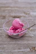Beautiful, fresh, pink ice cream and spoon in the transparent bowl, on the wooden surface