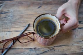 mug with Coffee in male hand on wooden table