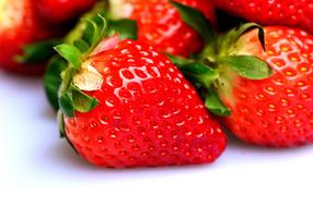 Beautiful, shiny, ripe, red strawberries, with the green leaves, on the white table, in light