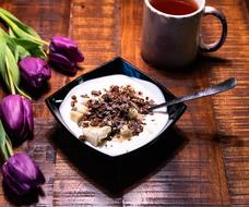 Beautiful yogurt with banana and muesli, violet tulip flowers and a cup of tea on the wooden table