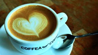 Cup of coffee, with beautiful heart drawing, on the saucer with shiny spoon, on the wooden table