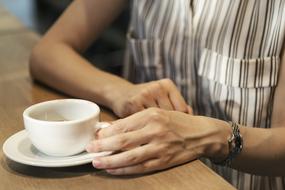 white cup in female hands on table