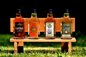 Colorful and beautiful bottles with rum, on the wooden bench, above the colorful grass