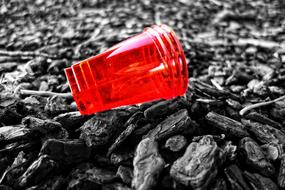 Close-up of the shiny, red plastic cup on the pebbles in black and white colors