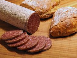 Beautiful still life with the cut sausage and fresh bread, on the wooden surface