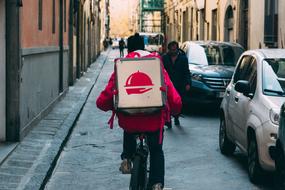 Foodora delivery guy cycling on bicycle, on the street with people, cars and buildings