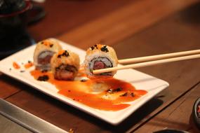 Close-up of the beautiful and colorful sushi rolls and chopsticks, on the white plae, on the wooden table