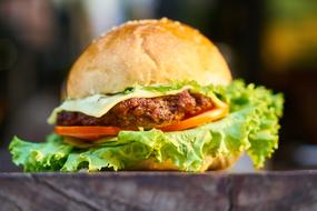 Close-up of the beautiful and colorful burger with meat and vegetables, on the wooden surface in light