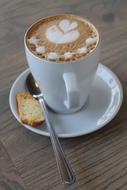 Cup of coffee with the beautiful drawing, on the saucer with biscuit and spoon