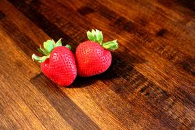 a pair of ripe strawberries on a wooden table