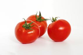Beautiful, shiny, ripe, red tomatoes with green leaves, on white surface