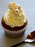 Close-up of the beautiful, yellow and brown cupcake in the paper, near the shiny spoon, on the wooden surface