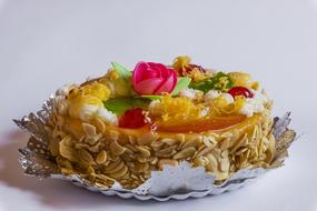 Close-up of the beautiful and colorful cake with fruits and flower with green leaves, on white surface