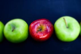 red Apple among green ones at dark background