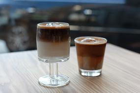 Two, shiny glasses with colorful coffee, on the wooden table
