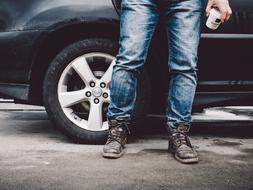 Man in jeans, with coffee cup, near the shiny car