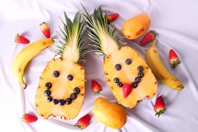 Beautiful pineapples with smiling faces, among the other colorful fruits, on the white cloth