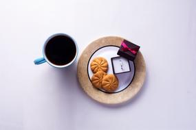 a cup of coffee, cookies, a ring in a box on a plate