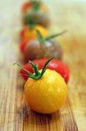 different tomatoes in a row on a wooden cutting board in a blurred background