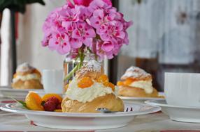 Beautiful and colorful cream puffs with fruits and berries near the vase with water and colorful flowers