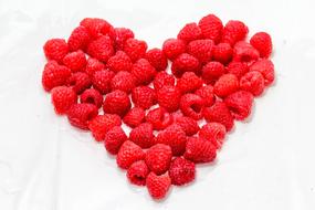 Beautiful heart shape made of the red raspberries, in light, on the white surface